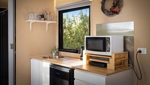 A compact kitchen with a built-in microwave, a small sink, and a window with a view of greenery. - Manna Gum Retreat by Tiny Away (Cudgee)