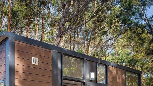 A modern cabin with a wooden exterior, large glass doors, and a wooden deck. - Manna Gum Retreat by Tiny Away (Cudgee)