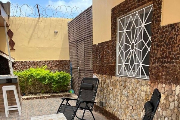 A patio area with a stone wall, a window with a geometric pattern, and two black chairs. - Sendou Cabano Villa Sleeps 6 With Parking (Sendou)