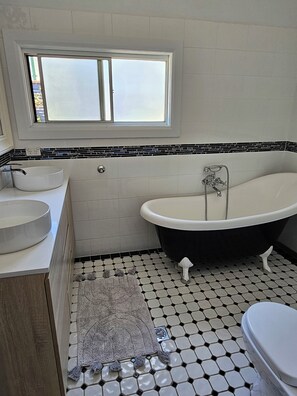 Un bagno con una vasca freestanding, un lavabo rotondo e una finestra sopra il lavabo.