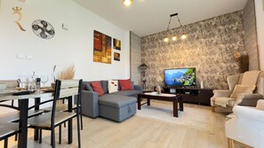 A living room with a sofa, a dining table with chairs, a television, and a stone wall.