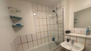 Kylpyhuoneessa on kylpyamme, pesuallas ja lasiseinällä varustettu suihku. Siellä on myös hyllyjä, joilla on hygieniatuotteita, ja peili pesualtaan yläpuolella.