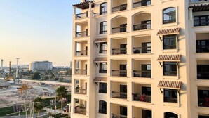 A multi-story building with balconies, a construction site in the background, and a clear sky.