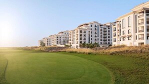 A golf course with a well-maintained green and a row of multi-story residential buildings in the background.