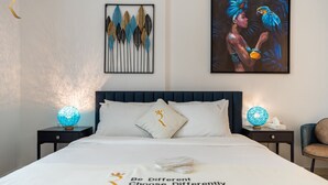 Une chambre d’hôtel avec un lit, deux tables de chevet, une tête de lit bleue, des œuvres d’art décoratives au mur et un tableau encadré.
