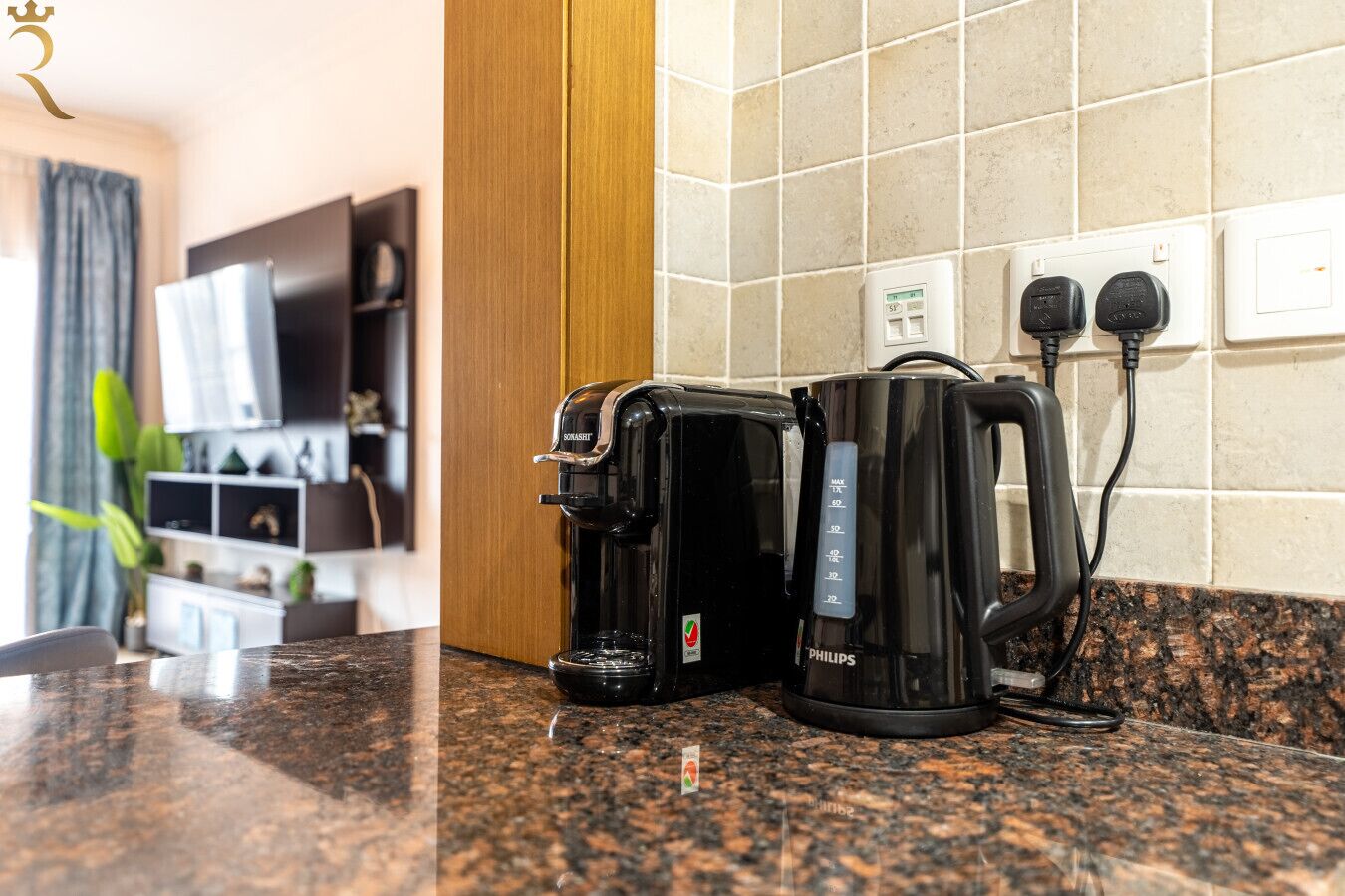 Eine Küche mit Kaffeemaschine und Wasserkocher auf einer Granitarbeitsplatte, einer Steckdose und einer Wandsteckdose.