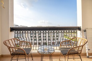 A balcony with wicker chairs, a glass table, and a view of a building.