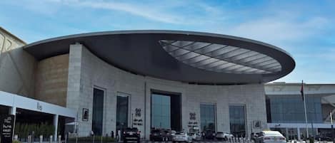 A modern building with a curved roof and large windows, a parking area with marked spaces, and a clear sky.