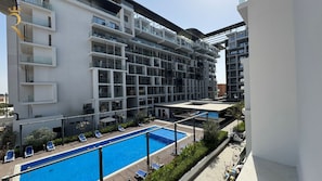 Un immeuble moderne à plusieurs étages, doté d’une piscine, de balcons et d’un espace extérieur couvert.