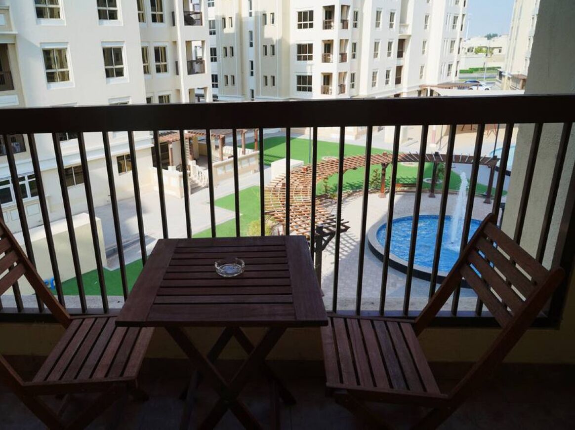 Een balkon met twee houten stoelen en een tafel, met uitzicht op een zwembad en een groen gazon.