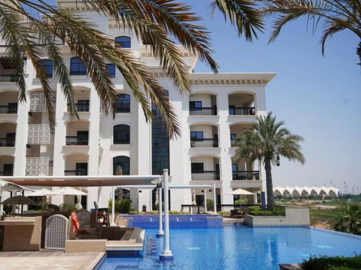Un hotel con piscina, palmeras y un edificio de varios pisos con balcones.