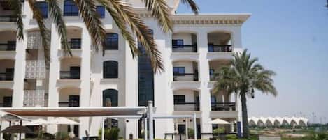 A hotel with a swimming pool, palm trees, and a multi-story building with balconies.