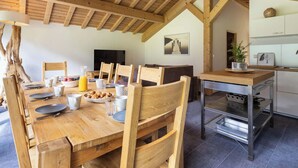 Un comedor con una mesa de madera dispuesta para cuatro personas, rodeada de sillas de madera. Se ve un área de cocina a la derecha, con un lavamanos y armarios.