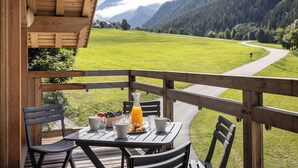 Una terraza de madera con una mesa dispuesta para el desayuno, con vistas a un paisaje montañoso y un camino sinuoso.