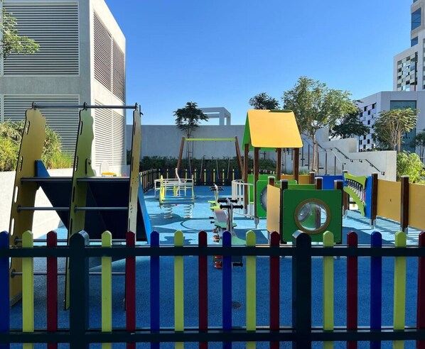 Un parque infantil con diversas estructuras de juego y una cerca de barras verticales coloridas.