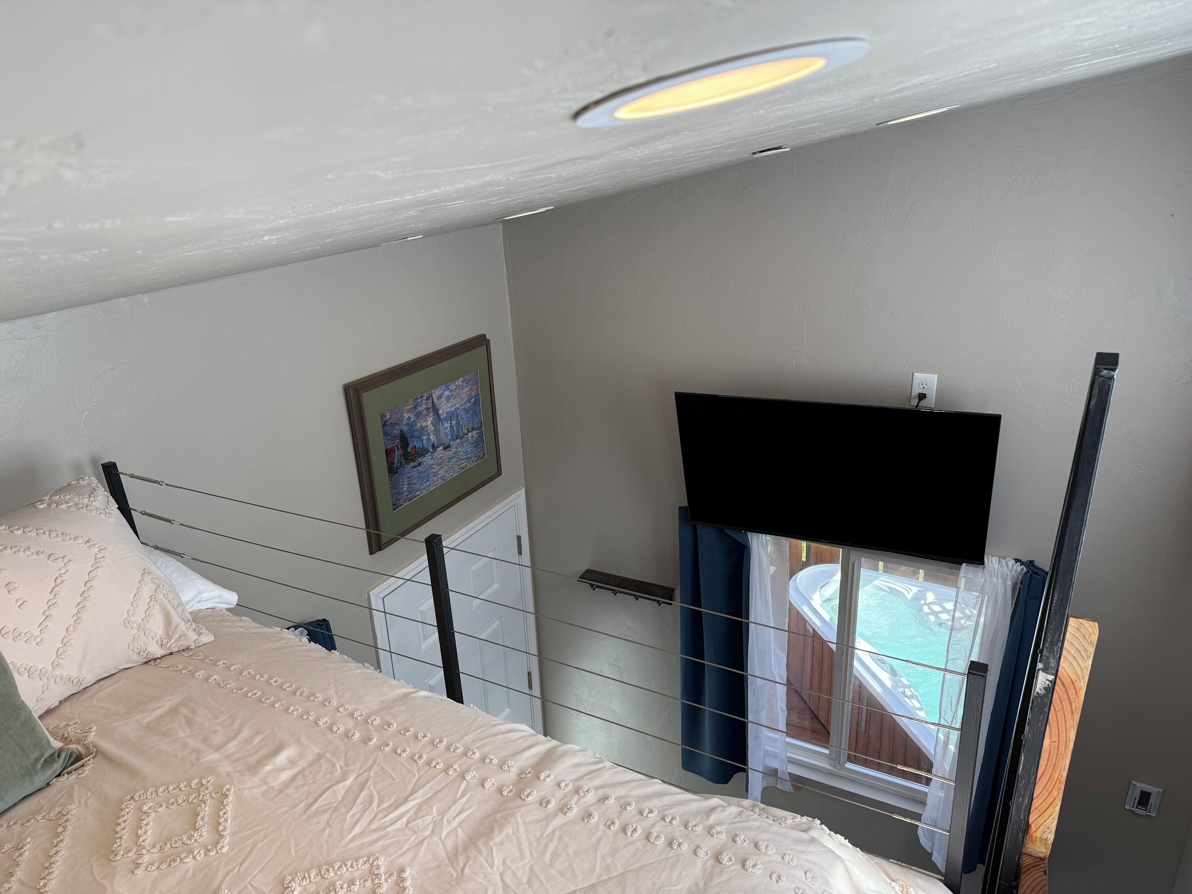 Une chambre à coucher avec un lit, un tableau, une télévision et une fenêtre avec des rideaux.