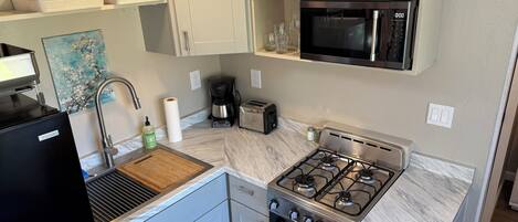A compact kitchen with a gas stove, oven, microwave, and a coffee maker.