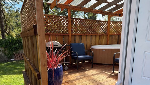 Un patio exterior con terraza de madera, un jacuzzi y dos sillas.