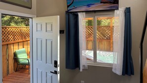 Una habitación con una puerta corredera que da a un balcón, un cuadro enmarcado sobre la puerta y un televisor en la pared mostrando una playa.