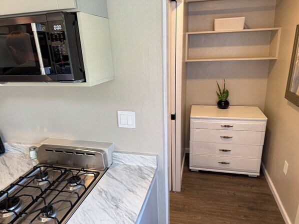 Una cocina compacta con estufa a gas, microondas y un mueble blanco.