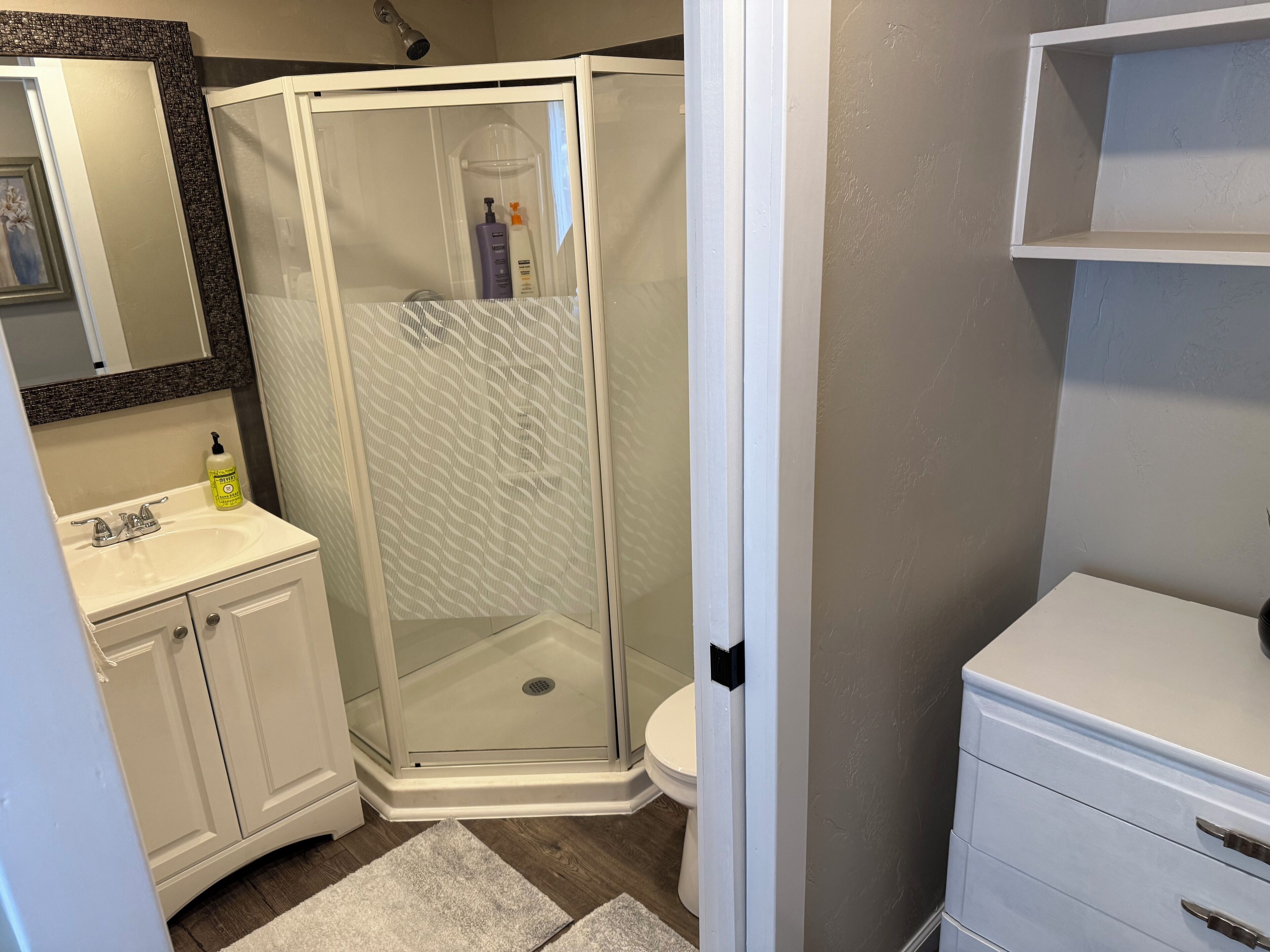 A bathroom with a shower, sink, toilet, and storage cabinet.