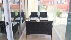 A balcony with wicker furniture and a glass door. - City Nest - 2BR apartment. (Abu Dhabi)