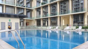 A swimming pool with lounge chairs and a glass railing. - Dainty 1BR Apartment in Masdar City (Abu Dhabi)