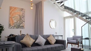 Uma sala de estar moderna com um sofá cinzento, um espelho redondo e uma escadaria para um andar superior.