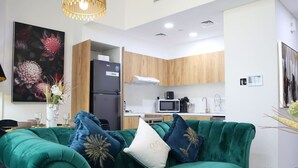 Un salon moderne avec un canapé de couleur turquoise, une table à manger et un coin cuisine doté de meubles en bois et d’un four à micro-ondes.