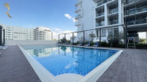 Una piscina con sillas de descanso y un edificio moderno al fondo.