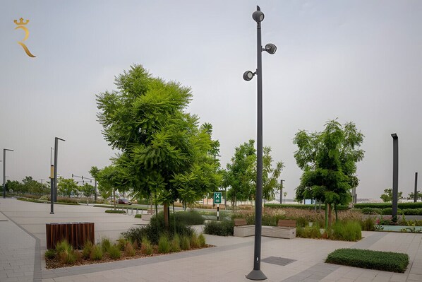 Zona urbana amb vegetació, fanal, arbres i un senyal verd.