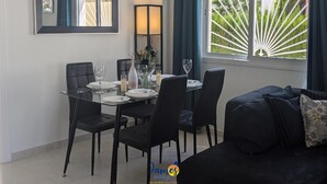 Spisestue med et bord dækket til fire personer, sorte stole, et bord af glas og udsigt til grøn vegetation gennem et vindue med hvide persienner.