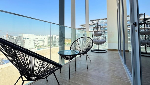 Un balcon doté d’une balustrade en verre, de deux chaises noires et d’un fauteuil suspendu avec un coussin.