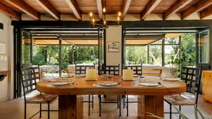 Comedor con mesa de madera dispuesta para cuatro personas, rodeada de sillas, con vista a follaje exterior.