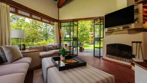 Ein modernes Wohnzimmer mit Sofa, Couchtisch und Kamin. Ein Fernseher ist an der Wand montiert und ein großes Fenster bietet Blick auf eine grüne Landschaft.