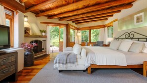 A cozy bedroom with a wooden ceiling, a large bed, a TV, and a fireplace. - Casas Abi: A Riverside Sanctuary with Firepit in Avándaro (Valle de Bravo)