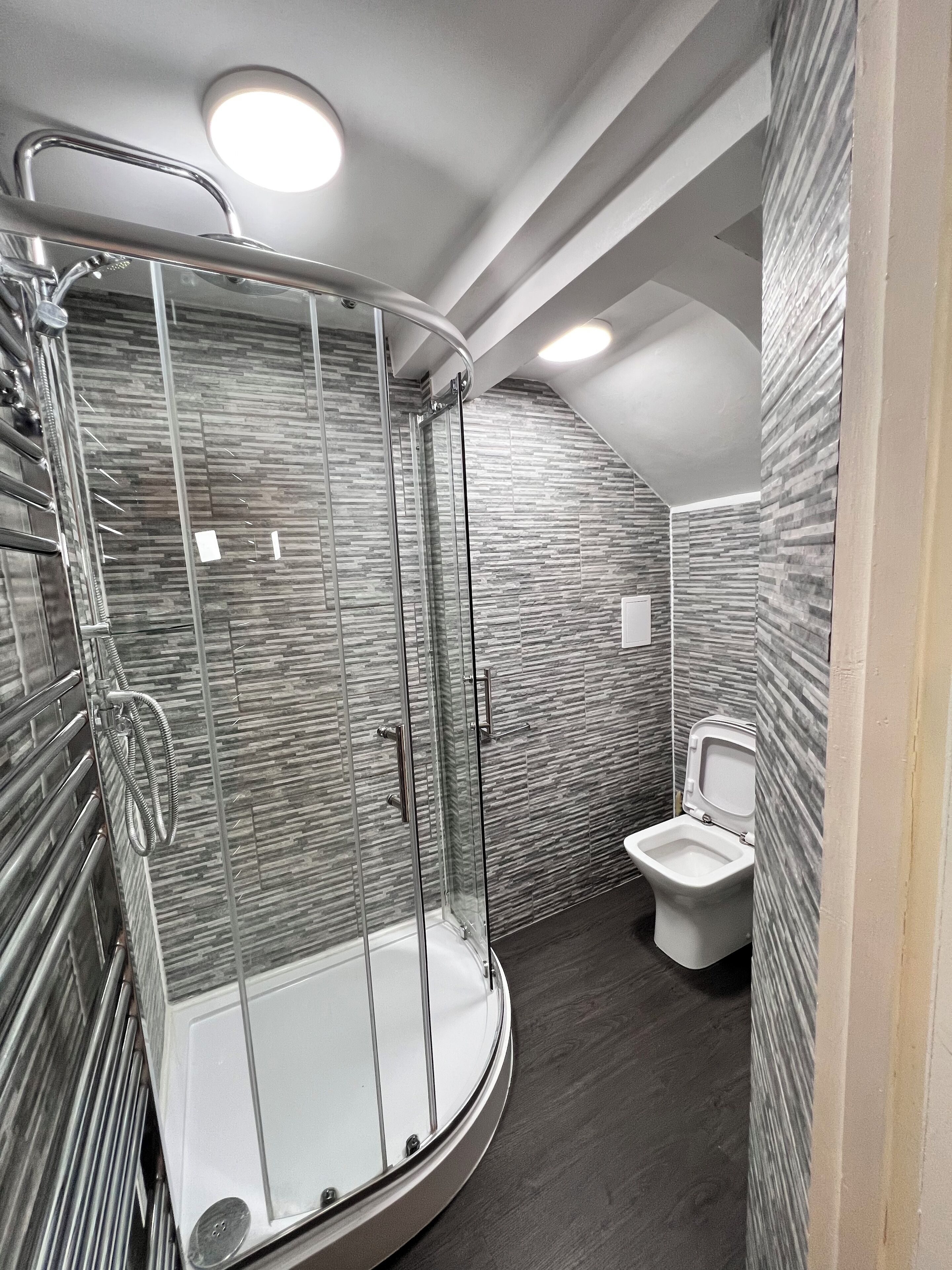 A modern bathroom with a glass-enclosed shower, a toilet, and a textured wall.