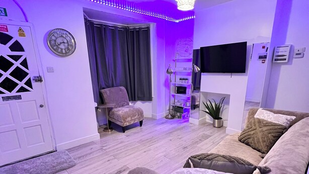 A modern living room with a plush sofa, a small armchair, a TV, and a fireplace. - Gillingham - 3 Beds - Sleeps 6 - Garden - Wifi (Gillingham)