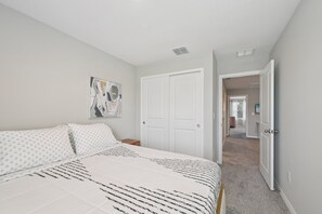 A bedroom with a bed, a white door, and a hallway leading to another room. - Comfortable 3-Bedroom Home – Sleeps 7 – Perfect for Vacation in Nokomis, FL (Nokomis)
