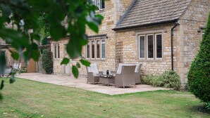 A stone building with a patio area featuring wicker furniture and a small table. - Arlington House - sleeps 6 guests  in 3 bedrooms (Lower Slaughter)
