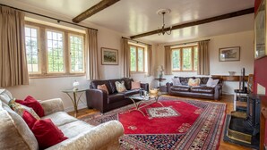A spacious living room with two sofas, a coffee table, and a fireplace. Large windows allow natural light to fill the room. - Arlington House - sleeps 6 guests  in 3 bedrooms (Lower Slaughter)