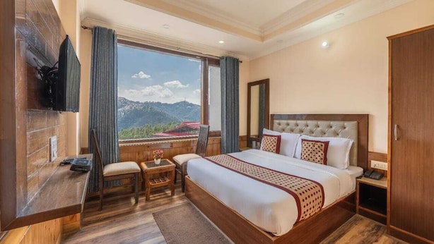 A hotel room with a large bed, a desk, a chair, a TV, and a wardrobe. - Hotel Charming Hills By Him Haults Hospitality (Shimla)