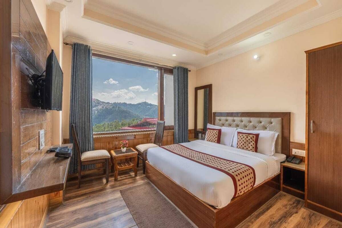 A hotel room with a large bed, a desk, a chair, a TV, and a wardrobe.