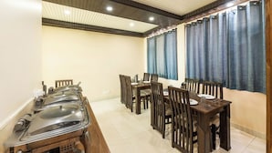 A dining area with a long table, multiple chairs, and a buffet setup. - Hotel Charming Hills By Him Haults Hospitality (Shimla)