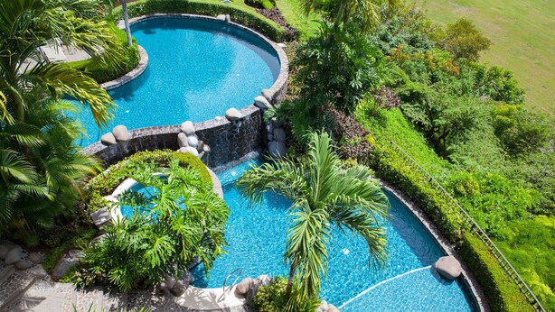 A circular pool with a stone wall and water feature, surrounded by lush greenery and palm trees. - Montebello 1E 3 bdr Ocean View in Los Suenos (Herradura Bay)