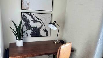 A workspace with a wooden desk, a brown leather chair, a potted plant, and two framed abstract artworks on the wall.