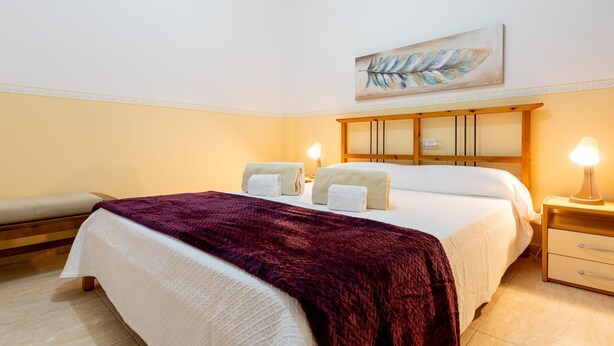 Una habitación de hotel con una cama grande, dos mesitas de noche, un banco y un cuadro en la pared.