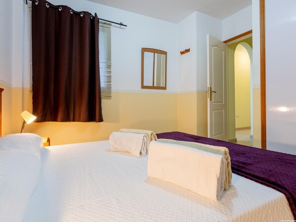 Habitación de hotel con una cama, una lámpara de noche, una ventana con cortinas, una puerta y un espejo en la pared.