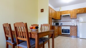 Un comedor con sillas de madera y una mesa, un frutero, armarios de madera, un microondas, un horno y un refrigerador.