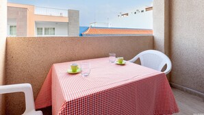Un balcón con mantel a cuadros, dos sillas y una mesa con dos tazas y un vaso.
